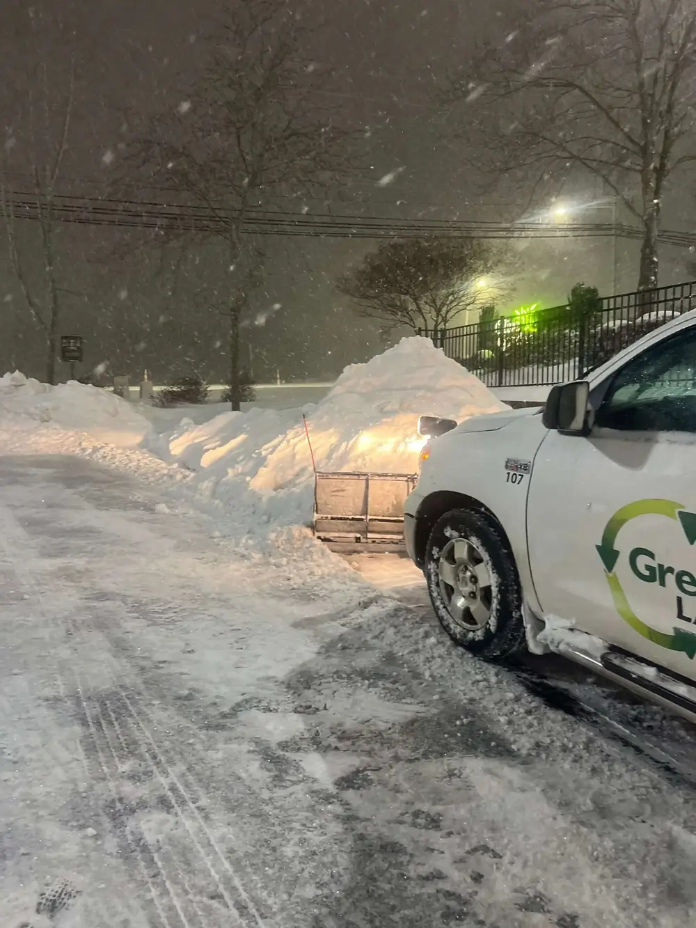 Green & Clean plow truck clearing snow at a commercial property at night